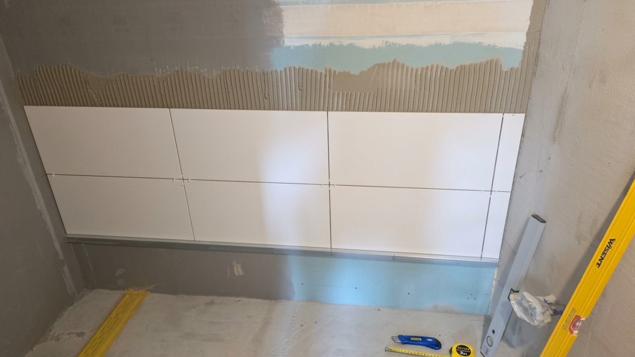 Verlegung großformatiger Wandfliesen auf der neu abgedichteten Wand, ausgerichtet an der Setzlatte.