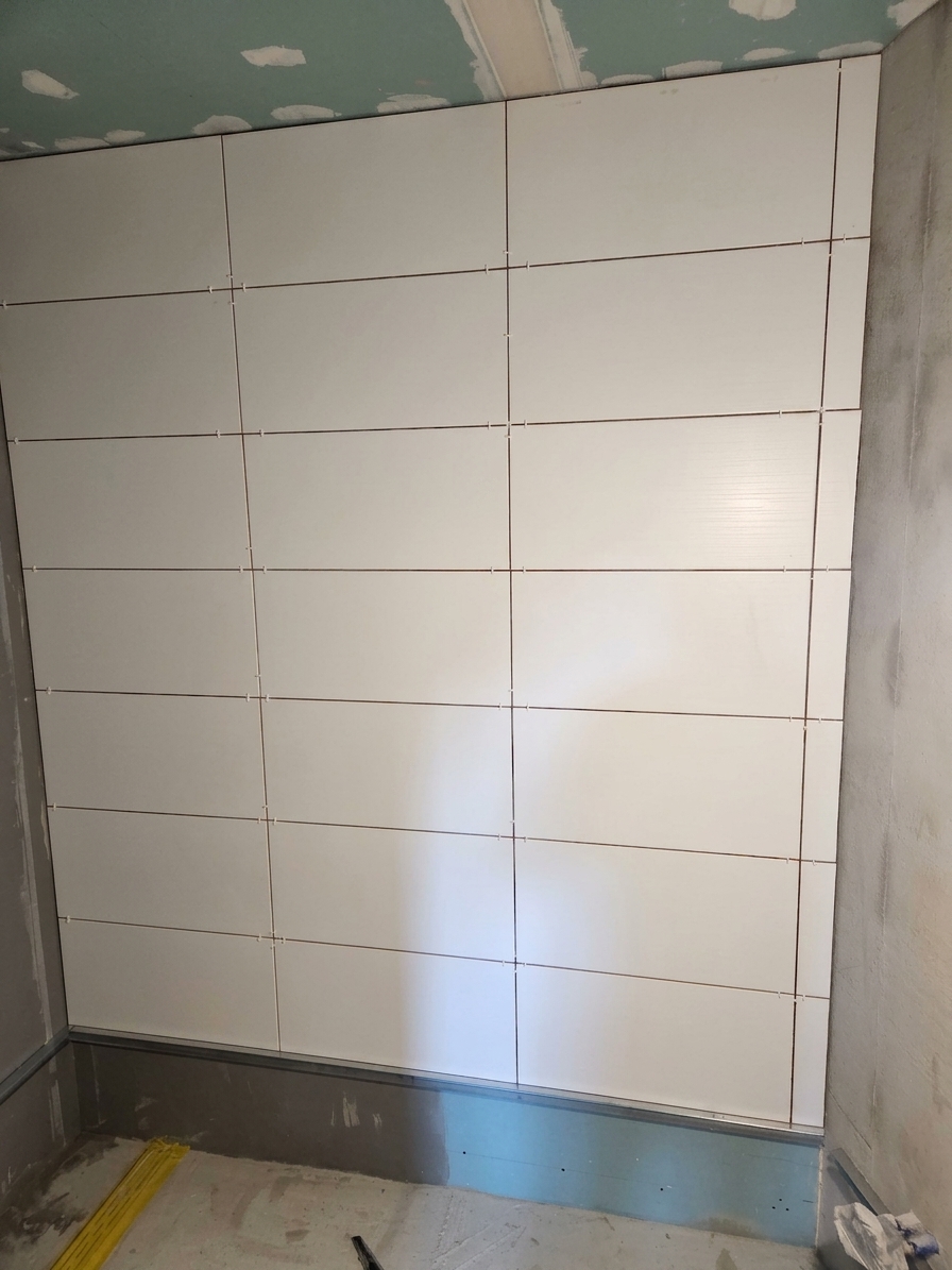 Die fertig geflieste Wand mit Sockelprofil; die Deckenanschlüsse werden noch gespachtelt.