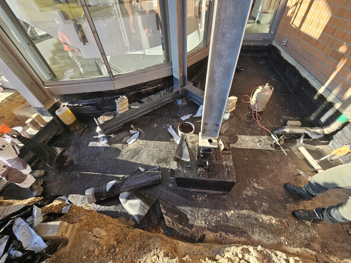 Verlegen der Bitumen-Schweißbahn auf der Deckenplatte, sauber an Stützen, Wand und Einläufe hochgeführt.