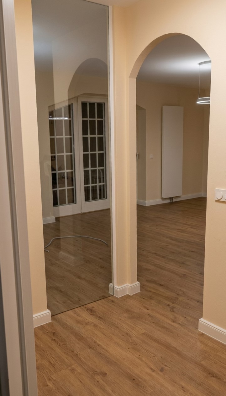 Blick durch den neuen Rundbogen: durchgehender Dielenboden und heller Wandton verbinden Flur und Wohnraum.