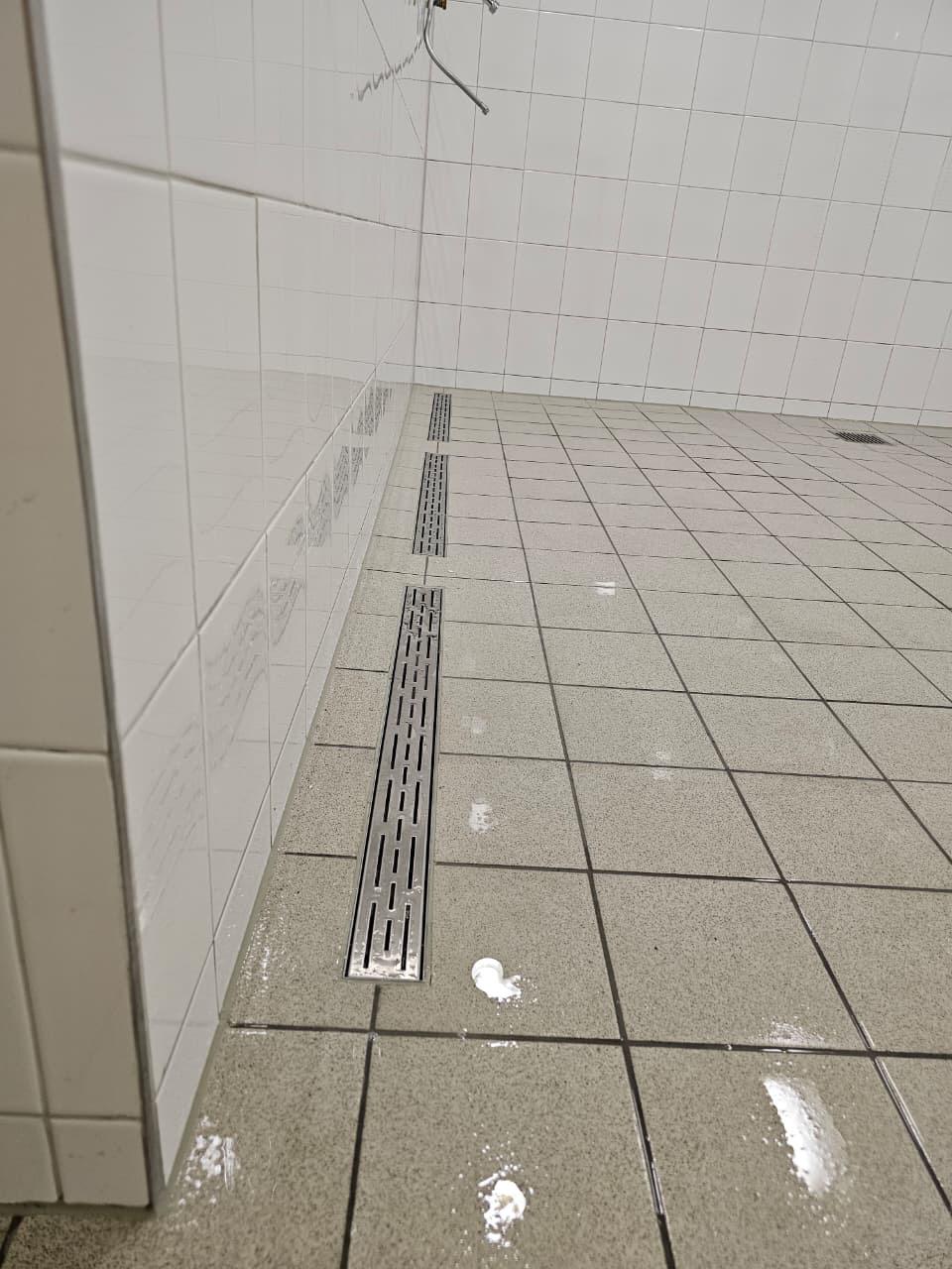 Detail der bodengleichen Entwässerung: Edelstahl-Rinnen entlang der Wand, frisch verfugt.